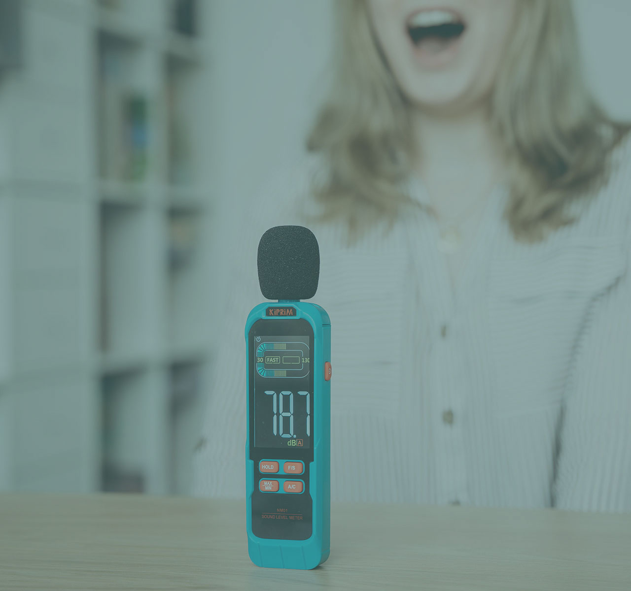 Ein Schallpegelmessgerät steht auf einem Tisch, während eine Person im Hintergrund eine Stimmübung ausführt